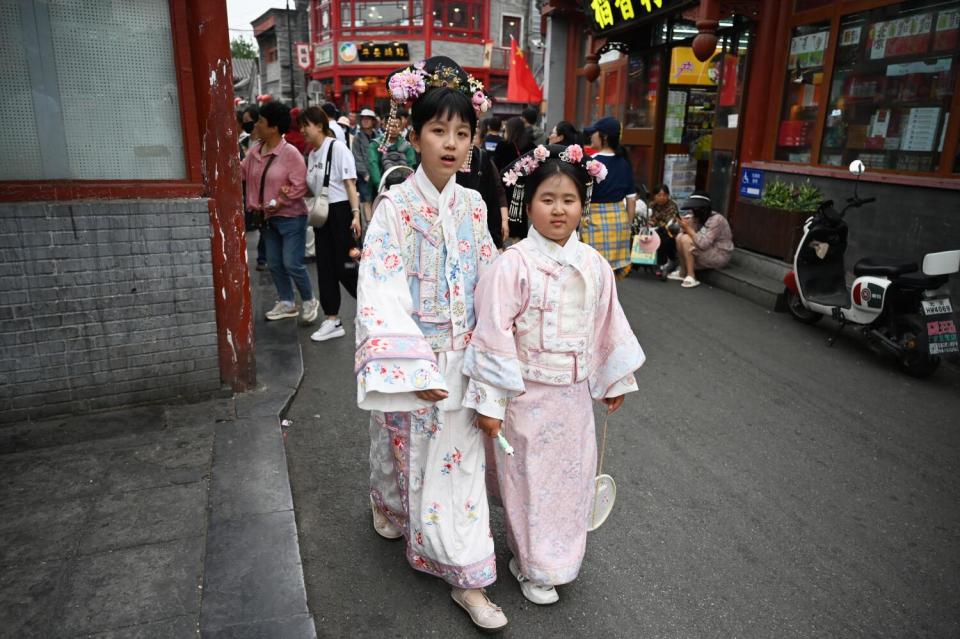Two girls wearing traditional flowing robes in pastel colors walk in a tourist shopping area