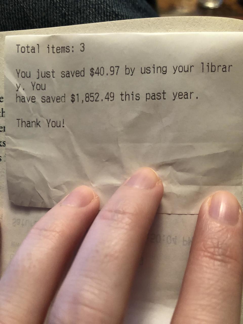 A handheld receipt showing the message "You just saved $41 by using your library; you have saved $1,853 this past year; thank you!"