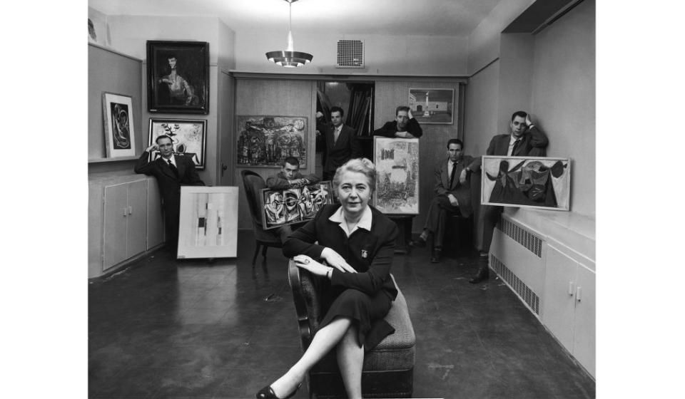 Edith Halpert at the Downtown Gallery, wearing the 13 watch brooch and ring designed for her by Charles Sheeler, in a photograph for <i>Life</i> magazine in 1952. She is joined by some of the new American artists she was promoting that year: Charles Oscar, Robert Knipschild, Jonah Kinigstein, Wallace Reiss, Carroll Cloar, and Herbert Katzman.