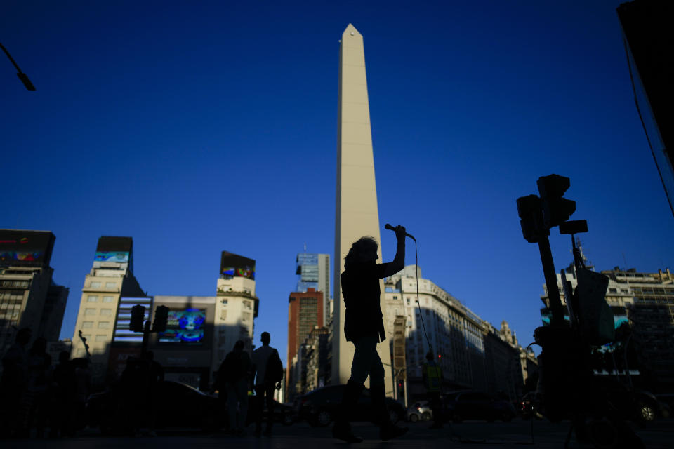 Retiree Ámbar Imoberdoff is silhouetted against the iconic obelisk monument as she performs for tips on a street corner in downtown Buenos Aires, Argentina, Thursday, March 7, 2024. Thanks to her impromptu recitals, Imoberdoff, who is a widow and has no children, says she can earn up to $200 on a good night during the weekends.. (AP Photo/Natacha Pisarenko)