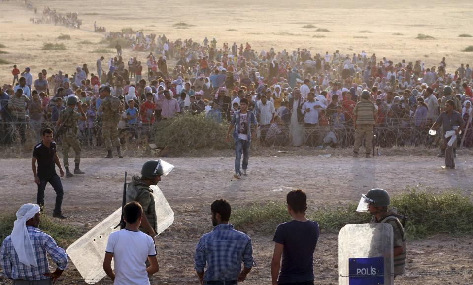 Turkish security forces stand guard as Syrians wait behind the border fences near the southeastern town of Suruc in Sanliurfa province, September 18, 2014. Islamic State fighters besieged a Kurdish city in northern Syria on Thursday after seizing 21 villages in a major assault, prompting a call to arms from Kurds in neighbouring Turkey who urged followers to go and help resist the group's advance. The attack on the city of Ayn al-Arab, known as Kobani in Kurdish, came two days after the top U.S. military officer said the Syrian opposition would probably need the help of the Syrian Kurds to defeat Islamic State. About 3,000 men, women and children arrived at the Turkish border roughly 10 km (6 miles) from Kobani but were still waiting on the Syrian side after night fell, a Reuters witness said, as Turkish forces stopped the crowd from crossing. REUTERS/Kadir Celikcan (TURKEY - Tags: POLITICS CIVIL UNREST CONFLICT MILITARY)