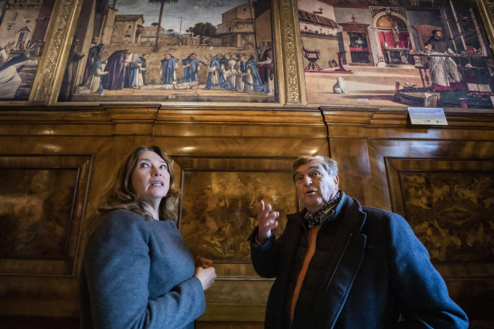 Piergiorgo Millich, guardián de la Escuela Dálmata, derecha, y Melissa Conn de la organización estadounidense sin fines de lucro Save Venice miran pinturas del artista renacentista Vittore Carpaccio en la planta baja de la Escuela Dálmata en Venecia el 7 de diciembre de 2022. A la izqueirda "El funeral de San Jerónimo", y a la derecha una réplica de "La visión de san Augustín", la pintura original, restaurada por Valentina Piovan, se encuentra en la Galería Nacional de Washington. (Foto AP/Domenico Stinellis)