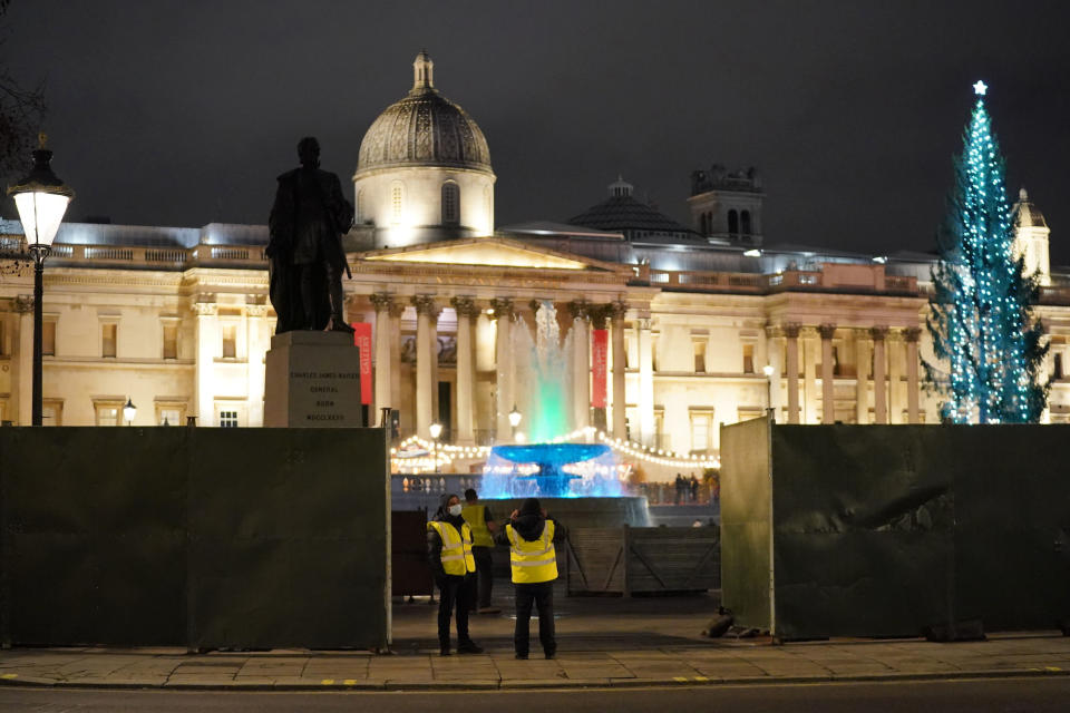 Security guards stand next to a boarding that has been erected around the parameters of Trafalgar Square, in London, Thursday, Dec. 30, 2021. British Prime Minister Boris Johnson has resisted implementing new restrictions on business and social interactions during the holiday season, instead emphasizing an expanded vaccine booster program to control the spread of omicron. (Jonathan Brady/PA via AP)