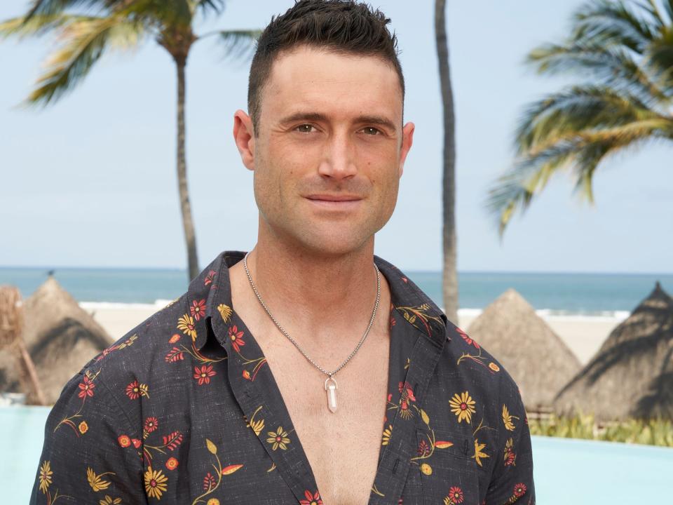 Aaron Schwartzman poses in a patterned shirt in front of a pool with a beach behind it.