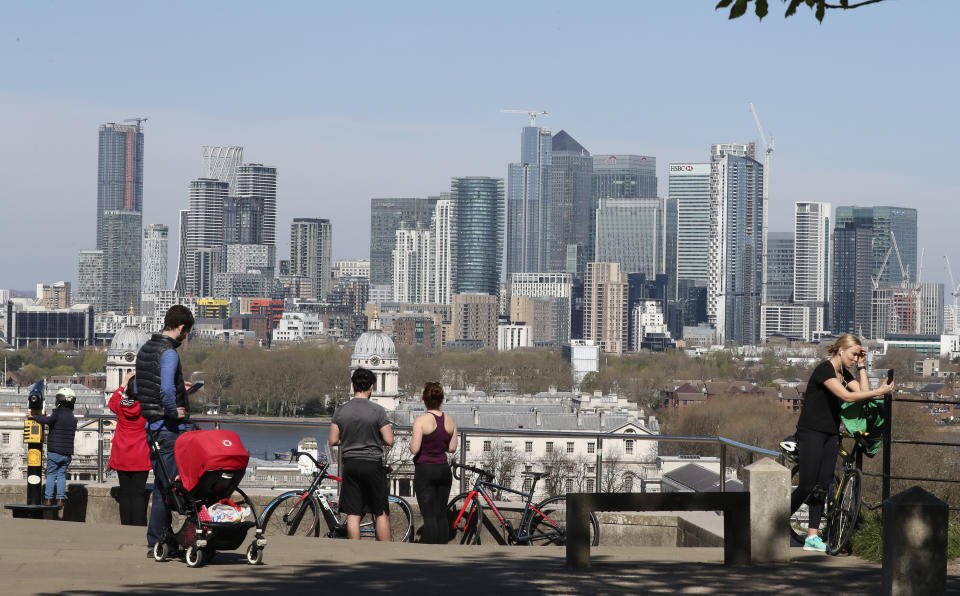 People stand on the upper section of Greenwich Park overlooking the Canary Wharf skyline, as another London park closed yesterday with most parks remaining open with the warning that they will close if people fail to observe the British government guidelines to help stop the spread of coronavirus, Sunday, April 5, 2020. The new coronavirus causes mild or moderate symptoms for most people, but for some, especially older adults and people with existing health problems, it can cause more severe illness or death. (AP Photo/Tony Hicks)