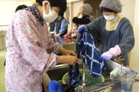 In this image from video, members of Japan Blue wash off dyed handkerchiefs at a community center which was used as an evacuation center when the massive earthquake hit the area in 2011, in Minamisoma, Fukushima Prefecture, northeastern Japan, on Feb. 21, 2021. Because of radiation released by the Fukushima nuclear plant disaster a decade ago, farmers in nearby Minamisoma weren't allowed to grow crops for two years. After the restriction was lifted, two farmers found an unusual way to rebuild their lives and help their destroyed community. They planted indigo and soon began dying fabric with dye produced from the plants. A group called Japan Blue holds workshops that have taught indigo dyeing to more than 100 people each year. (AP Photo/Chisato Tanaka)