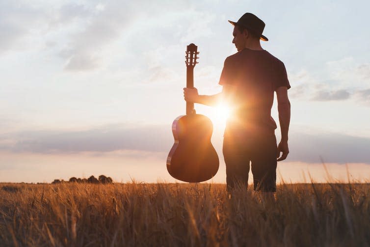 Silhouette of guitarist in field at sunset.