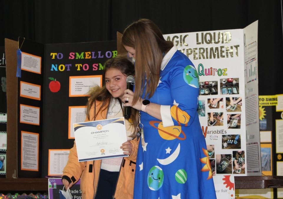 St. James Lutheran School science teacher Leah Sinke (dressed as Ms. Frizzle from the popular children's science show "The Magic School Bus") presents a "Champion Award" to second-grader Sofia Quiroz on Thursday, Jan. 18, 2024. Quiroz was the only student in the school to voluntarily participate in the science fair this year.