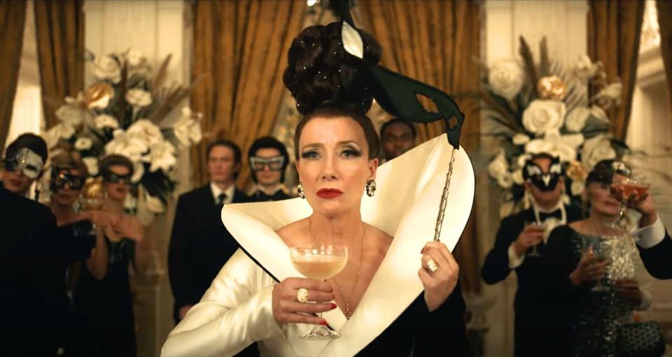 emma thompson holding a glass of champagne and a mask in disney's cruella