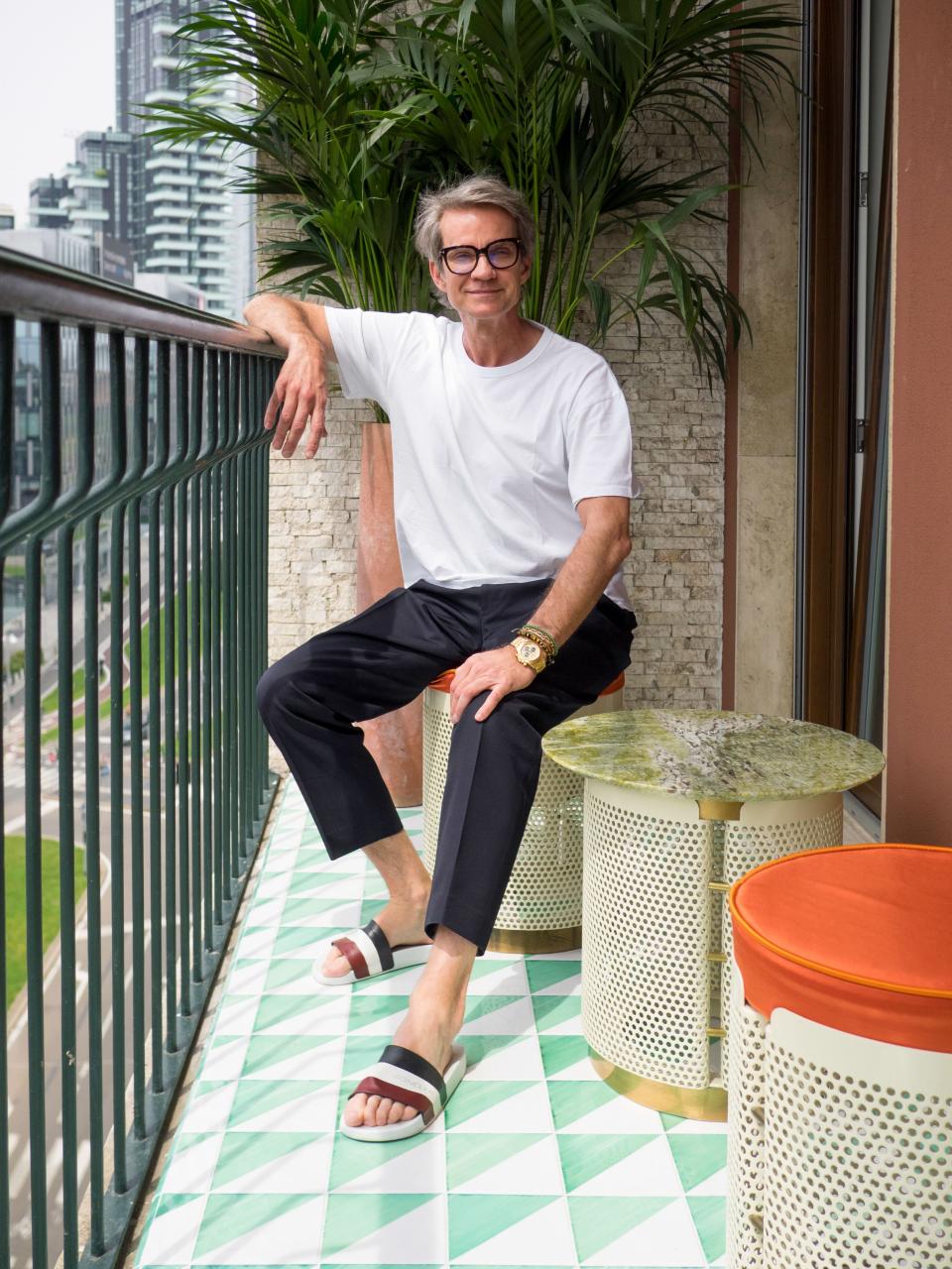 Alexander Werz, co-CEO of Karla Otto, sits on the terrace of his Milan apartment; the tiles are leftovers from the Palazzo Butera in Palermo, and the stools and table are by Derek Castiglioni.
