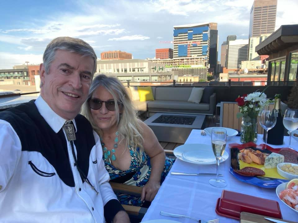 This July 3, 2020 image provided by Peter Batty shows him and his wife celebrating their anniversary and the opening night of the Santa Fe Opera on their balcony in Denver, Colo. The famed opera is offering a series of virtual performances after being forced to cancel the 2020 season due to the coronavirus pandemic. The Saturday night events are meant to celebrate the five originally-scheduled operas that would have been performed this summer. (Peter Batty via AP)