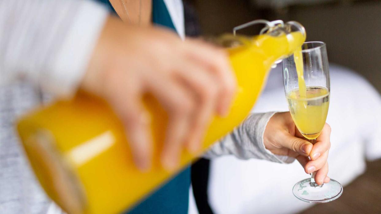 Woman pouring orange juice into champagne in glass to make mimosa