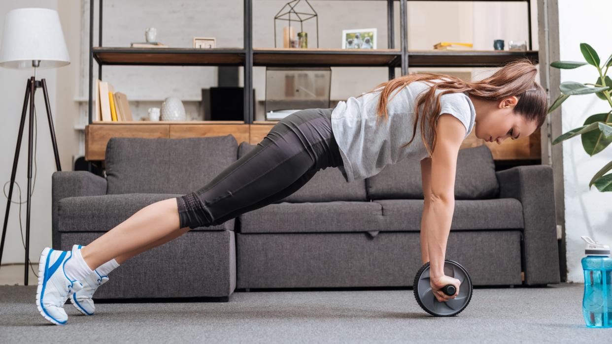  Woman at home doing an abs wheel plank . 