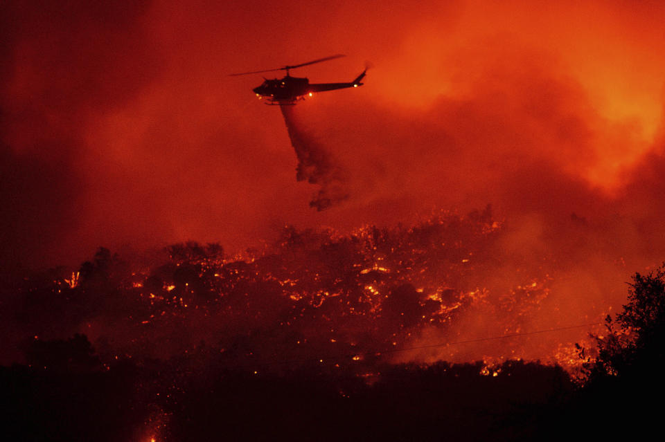 A helicopter drops water on the Cave Fire burning along Highway 154 in Los Padres National Forest, Calif., above Santa Barbara on Tuesday, Nov. 26, 2019. (AP Photo/Noah Berger)