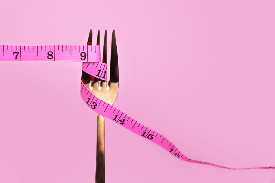 Pink measuring tape and fork on pink background. Slim concept. Healthy lifestyle.