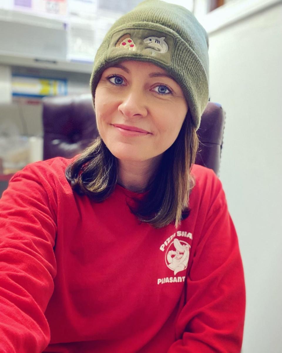 Sarah Koopman, co-owner of Pizza Shark Cape Cod, shows off a Pizza Shark sweatshirt in red. The cobalt blue version sold out after actress Meghann Fahy wore it in an Instagram post.