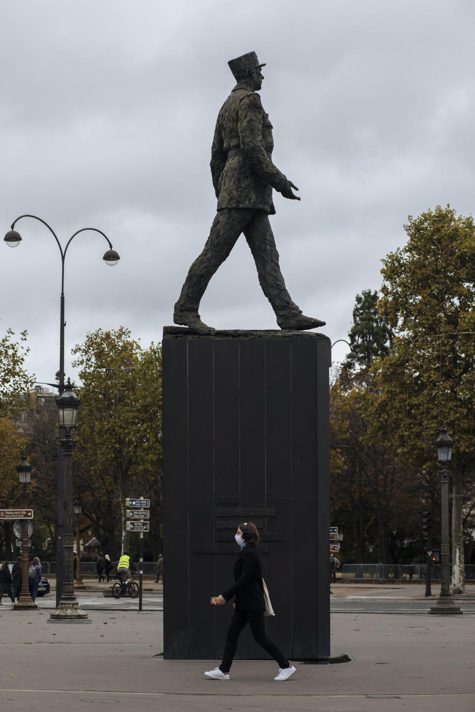 A woman wearing a mask walks by a General de Gaulle statue, on the Champs Elysees avenue in Paris, Sunday Oct.25, 2020. A curfew intended to curb the spiraling spread of the coronavirus, has been imposed in many regions of France including Paris and its suburbs. (AP Photo/Lewis Joly)