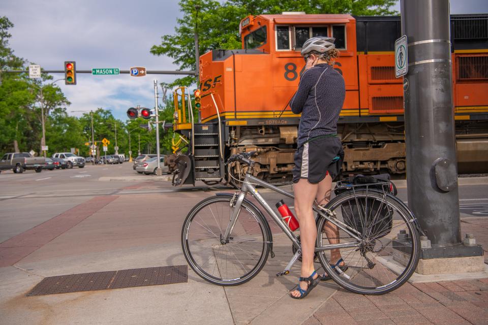 Bicyclist Sam Sickbert covers her ears as a train travels down Mason Street on Wednesday, June 26, 2019.  Sickbert waited to cross the street after visiting a Bike to Work Day station at Snooze an AM Eatery, on Mountain Ave. Bicyclists received free breakfast and treats at more than 68 stations located throughout Fort Collins. Bicycle mechanics  were located at several stations for minor repairs.