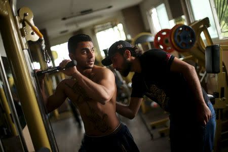 Palestinian artist Bilal Khalid paints Arabic letters on a bodybuilder in a gym in Gaza City April 12, 2016. REUTERS/Mohammed Salem