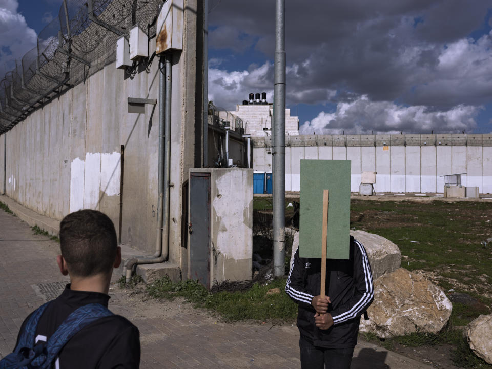 FILE - Palestinian students wait for transportation next to a section of Israel's concrete barrier separating between Jerusalem and the West Bank village of A-Ram, in Jerusalem, Feb. 3, 2022. (AP Photo/Oded Balilty, File)