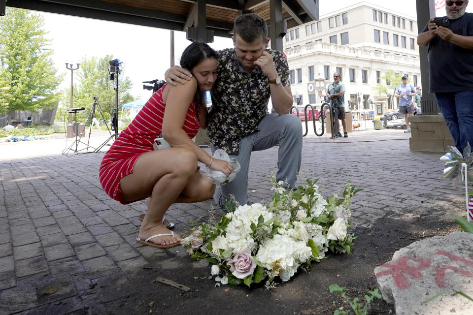 Brooke y Matt Strauss, que se casaron el domingo, hacen una pausa el martes 5 de julio de 2022 después de dejar sus ramos de boda en el centro de Highland Park, Illinois, un suburbio de Chicago, cerca de la escena de la masacre del lunes. (AP Foto/Charles Rex Arbogast)