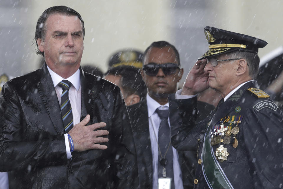 En esta imagen de archivo, tomada el 17 de abril de 2019, el presidente de Brasil, Jair Bolsonaro, se lleva la mano al corazón y el comandante del ejército Edson Leal Pujol hace un saludo militar durante la interpretación del himno en una ceremonia, celebrada bajo un intenso aguacero, para conmemorar el Día del Ejército, en Brasilia, Brasil. En el inicio de su segundo año como presidente, Bolsonaro se ha mantenido firme en sus combativas políticas mientras se enfrentó a sus críticos tanto dentro como fuera del país. (AP Foto/Eraldo Peres, archivo)