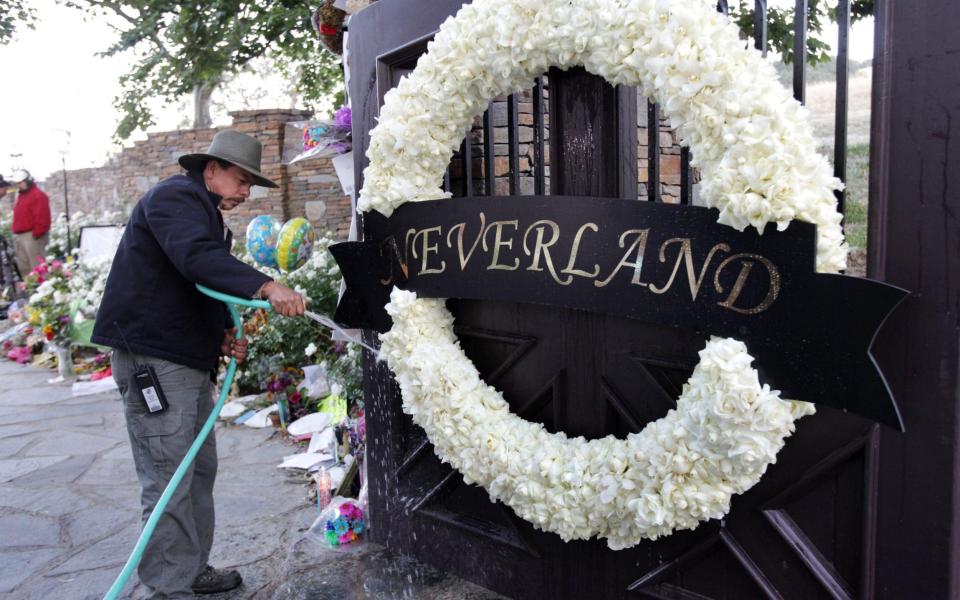 A worker waters thewreath of white roses on the Neverland Ranch gate in 2009 - ap