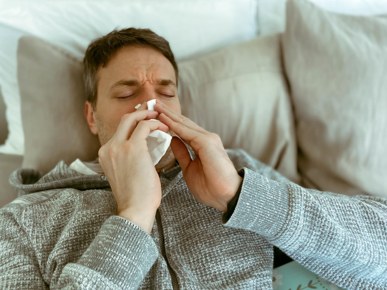 Mid adult man feeling under the weather sneezes in bed