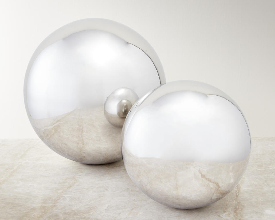 This image provided by CB2 shows festive decorations made of made of glass, resin and metal. CB2 has a new collection of transparent, opaque, and reflective glass and metallic ornaments that give traditional holiday icons like gift boxes, snowmen, trees and reindeer a fresh twist. There are trees made of clear and amber glass balls that look like bubbly champagne; a trio of modern pines in smoky hues; milky white glass snowmen; stainless steel orbs; and mini presents in mirror-finished steel. (CB2 via AP)