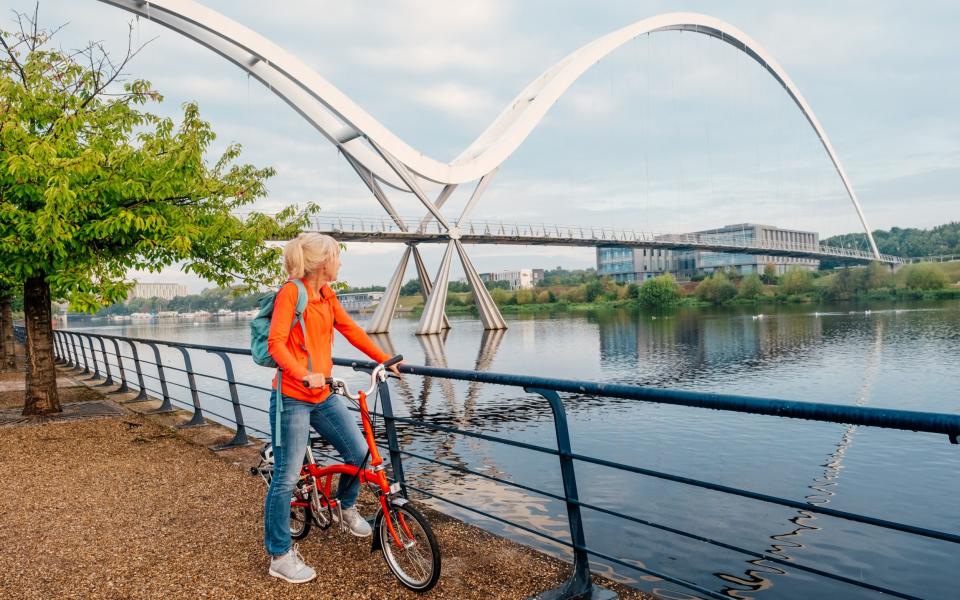 Woman on the promenade with her bicycle pausing to view the Infinity Bridge at Stockton on Tees, England.