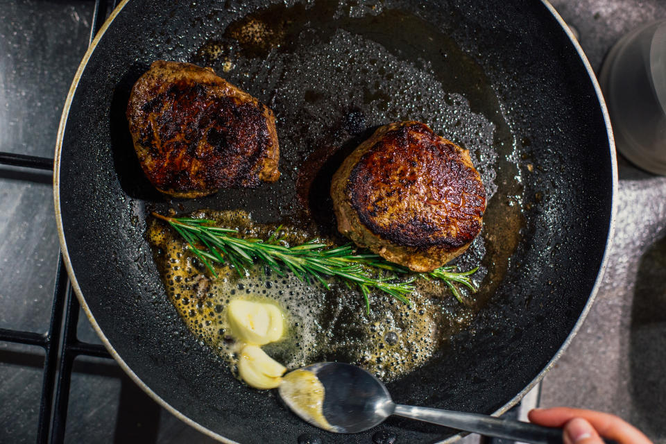 a steak being basted in a pan with butter and herbs