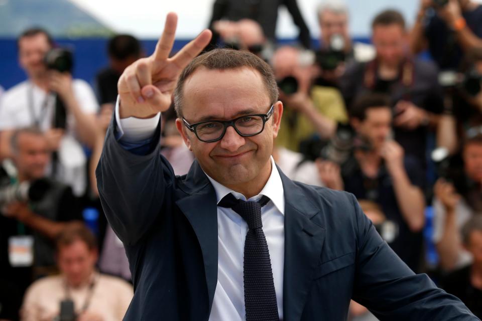 A man in a suit holds up a peace sign as people are seen behind him.