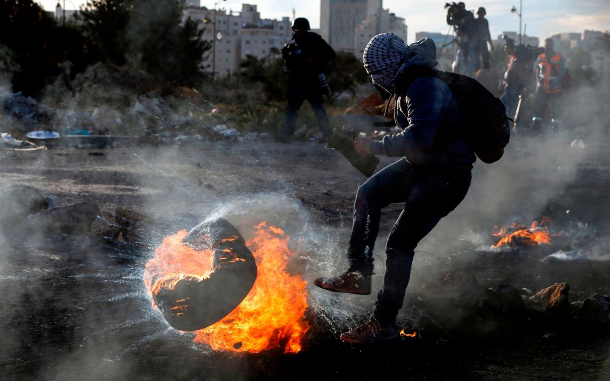 A Palestinian protester kicks a flaming tire during clashes with Israeli forces in the West Bank city of Ramallah on Monday - AFP