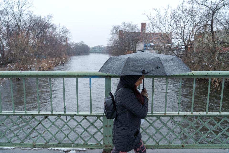 A woman walks along Bridge St over the Passaic River in Paterson, NJ on Tuesday Jan. 9, 2024. The Passaic River is expected to flood during the rainstorm arriving Tuesday night, into Wednesday.