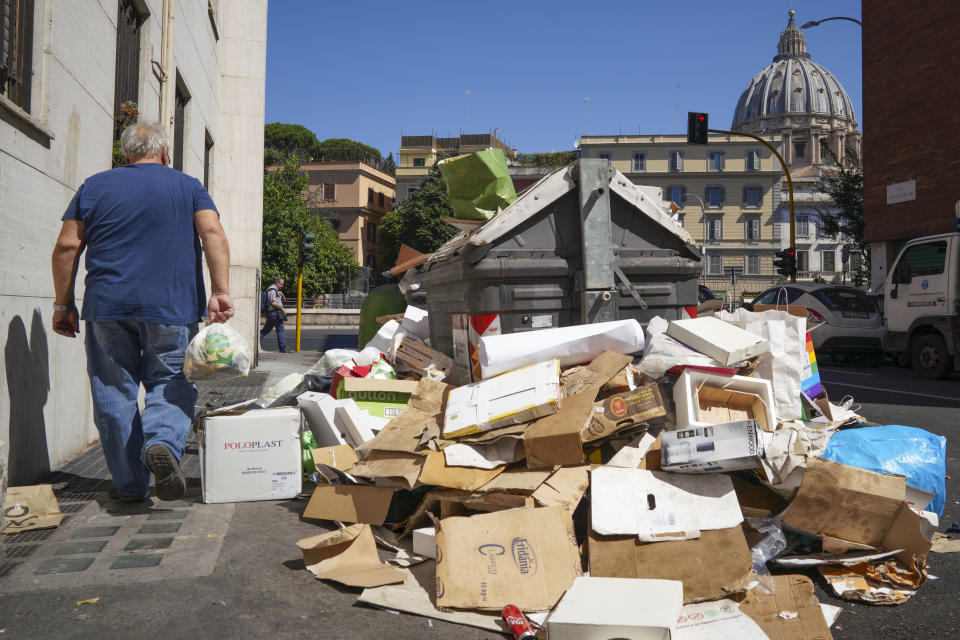 In this photo taken on Monday, June 24, 2019, a man walks past a pile of garbage as St. Peter's Dome is visible in background, in Rome. Doctors in Rome are warning of possible health hazards caused by overflowing trash bins in the city streets, as the Italian capital struggles with a renewed garbage emergency aggravated by the summer heat. (AP Photo/Andrew Medichini)