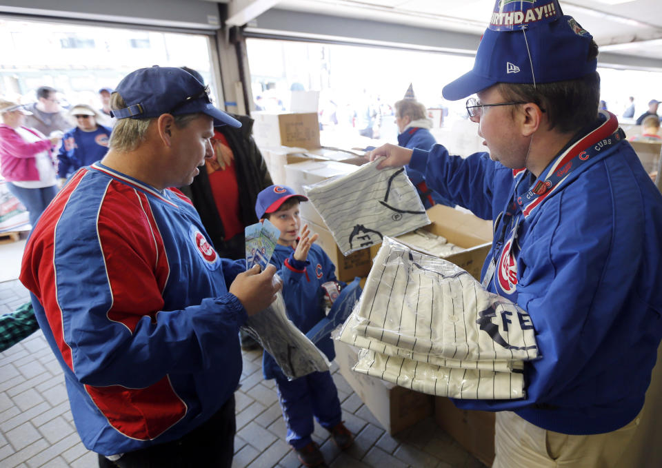 Usher John O'Brien, right, hands out the 1914 replica Chicago Federals' jersey to fans for the 100th anniversary of the first baseball game at Wrigley Field, before a game between the Arizona Diamondbacks and Chicago Cubs, Wednesday, April 23, 2014, in Chicago. (AP Photo/Charles Rex Arbogast)