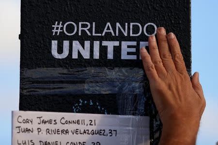 A person rubs an "#Orlando United" sticker on the sign pole outside Pulse nightclub following the mass shooting last week in Orlando, Florida, U.S., June 21, 2016. REUTERS/Carlo Allegri