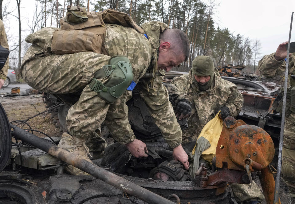 Soldados ucranianos intentan sacar el cadáver de un soldado ruso del interior de un tanque ruso destruido en la aldea de Dmytrivka cerca de Kiev, Ucrania, el sábado 2 de abril de 2022. (AP Foto/Efrem Lukatsky)