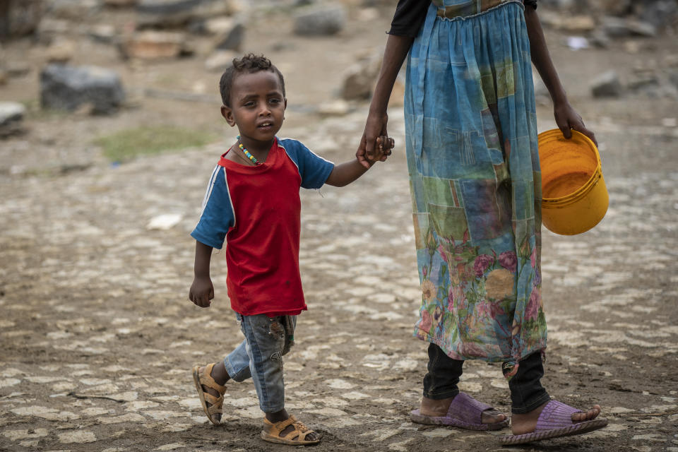 A displaced Tigrayan boy walks with a relative to receive food at the Hadnet General Secondary School which has become a makeshift home to thousands displaced by the conflict, in Mekele, in the Tigray region of northern Ethiopia Wednesday, May 5, 2021. The Tigray conflict has displaced more than 1 million people, the International Organization for Migration reported in April, and the numbers continue to rise. (AP Photo/Ben Curtis)