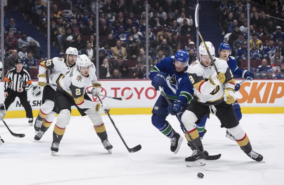 Vancouver Canucks' J.T. Miller, second from right, and Vegas Golden Knights' Jack Eichel, right, vie for the puck during the third period of an NHL hockey game Sunday, April 3, 2022, in Vancouver, British Columbia. (Darryl Dyck/The Canadian Press via AP)