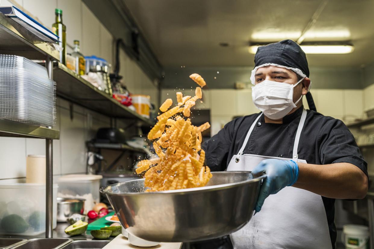 Chef seasoning french fries with salt in a bowl flipping them at the kitchen of restaurant.