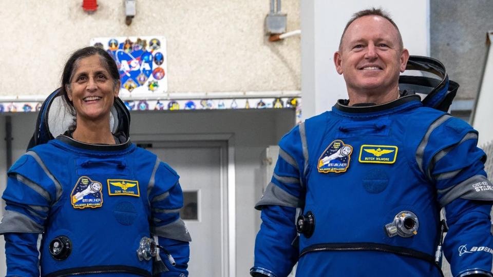 two astronauts stand and laugh in spacesuits