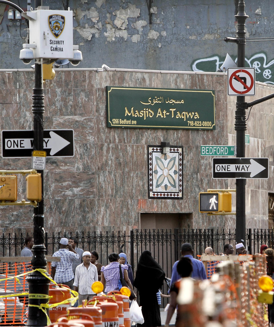 FILE - In this Aug. 18, 2011, file photo, people walk below a New York Police Department security camera, upper left, which was placed next to a mosque on Fulton Street in the Brooklyn neighborhood of Bedford-Stuyvesant in New York. On Tuesday, April 15, 2014, The New York City Police Department announced that it disbanded the unit tasked with monitoring Muslim communities in both New York and Newark, N.J. The program that relied on plainclothes officers to eavesdrop on people in bookstores, restaurants and mosques became the subject of two federal lawsuits. (AP Photo/Bebeto Matthews, File)