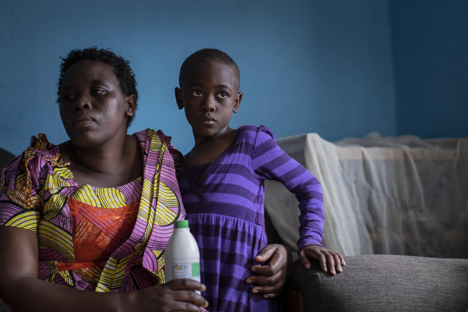 In this photo taken Wednesday, Nov. 6, 2019, mother Joselyne Mukanyabyenda, left, holds the bottle of oral liquid morphine that her daughter Ange Mucyo Izere, 6, right, uses to alleviate the pain of her bone marrow cancer, inside her home in the Gitega neighborhood of the capital Kigali, Rwanda. While people in rich countries are dying from overuse of prescription painkillers, people in Rwanda and other poor countries are suffering from a lack of them, but Rwanda has come up with a solution to its pain crisis - it's morphine, which costs just pennies to produce and is delivered to households across the country by public health workers. (AP Photo/Ben Curtis)