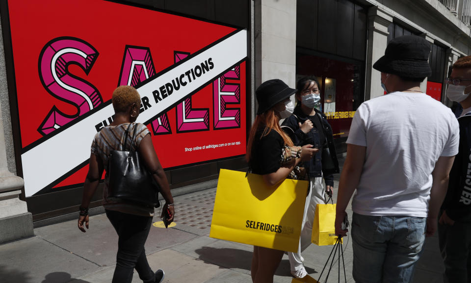 Shoppers stand in front of a large department store wearing masks in London, Thursday, July 23, 2020. Making masks mandatory in shops is "the right thing to do," Britain's Prime Minister Boris Johnson said Thursday, a day before new rules were set to come into force in England. (AP Photo/Alastair Grant)