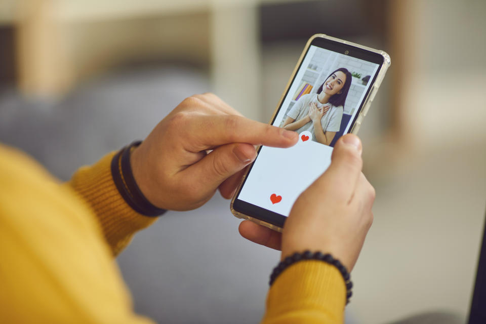 Dating app or site in mobile phone screen. Close up of a lonely man uses a smartphone to flip through women's profiles and presses a heart button with his finger. Banner or mockup website concept.