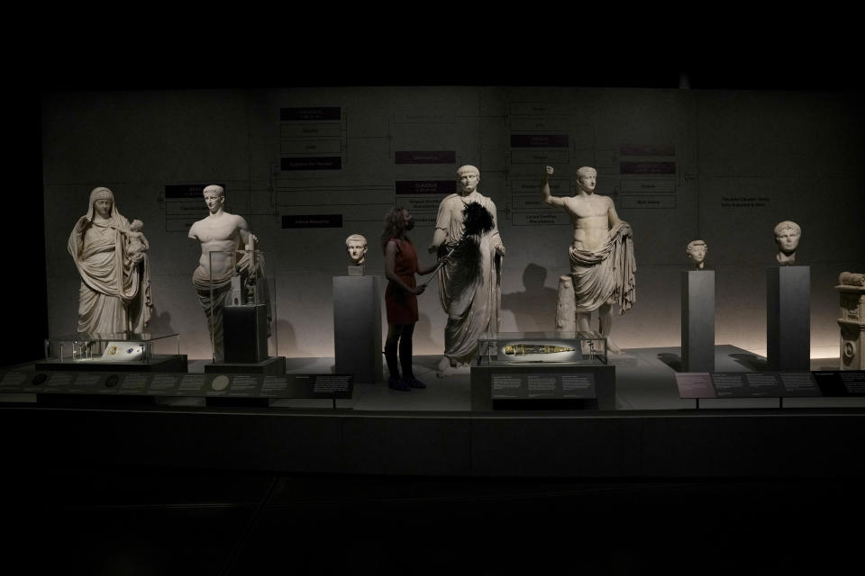 A museum employee poses for photographers with statues of members of the Julio-Claudian family which was from the first Roman emperor Augustus descending to Nero the last in the line, during a media preview for the "Nero: the man behind the myth" exhibition, at the British Museum in London, Monday, May 24, 2021. The exhibition, which open to visitors on May 27 and runs until October 24, explores the true story of Rome's fifth emperor informed by new research and archaeological evidence from the time. (AP Photo/Matt Dunham)