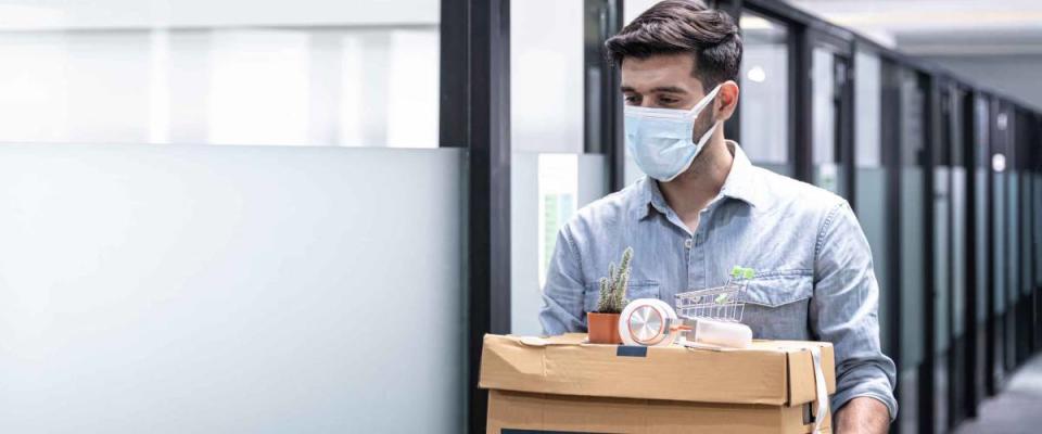 Man in mask leaving office with box of belongings