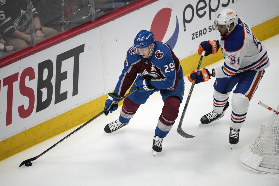 Colorado Avalanche center Nathan MacKinnon, left, looks to pass the puck as Edmonton Oilers left wing Evander Kane defends during the first period of an NHL hockey game Tuesday, April 11, 2023, in Denver. (AP Photo/David Zalubowski