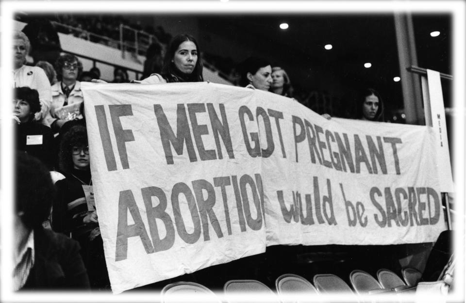 In the grandstand at the 1977 National Women's Conference, a group of women attendees hold a banner that reads 'If Men Got Pregnant Abortion Would Be Sacred,' Houston, Texas, November 1977. (Photo: National Commission for the Observance of the International Women's Year/PhotoQuest/Getty Images; digitally enhanced by Yahoo News)